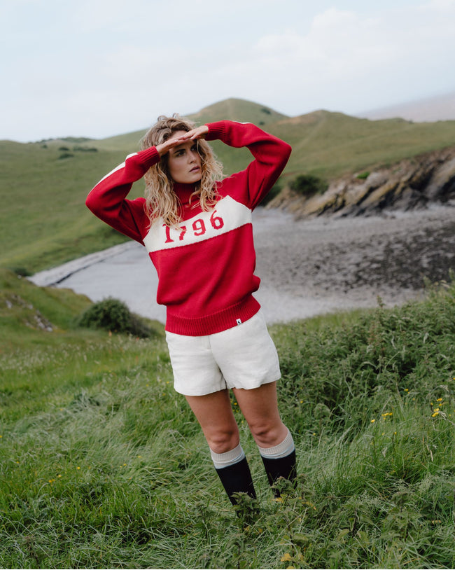 Person wearing a red and white sweatshirt with '1796' on a grassy field with a scenic background.
