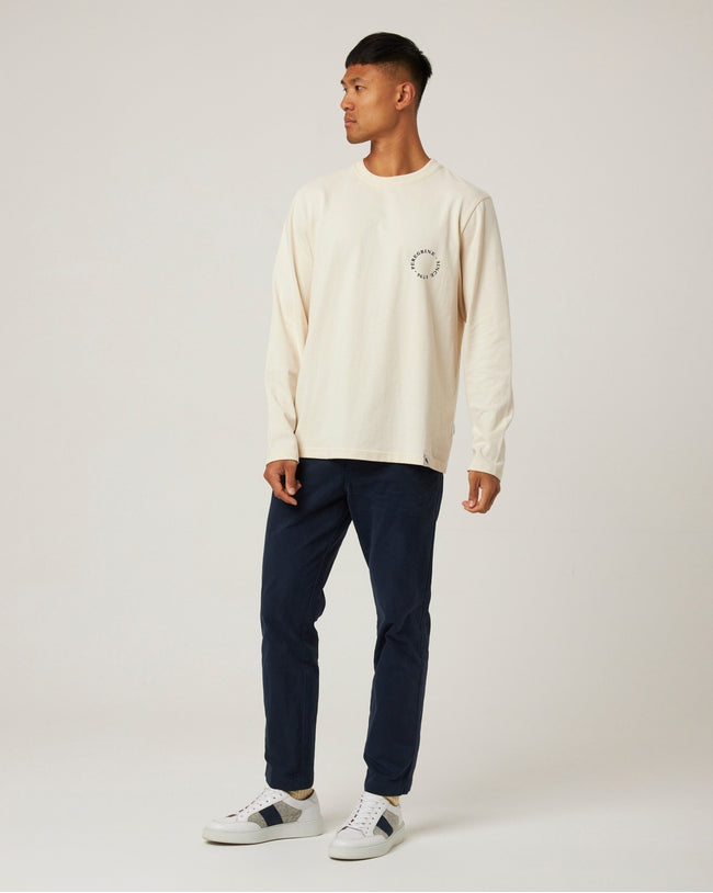 Man wearing a cream sweater and navy pants on a white background