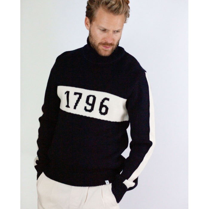 Flatlay image of 1796 navy merino wool knitted jumper. Navy jumper with white stripe across the chest detailing 1796 in navy 