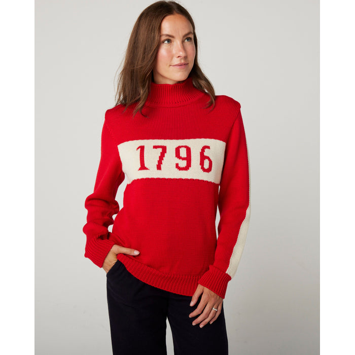 Flatlay image of 1796 red merino wool knitted jumper. red jumper with white stripe across the chest detailing 1796 in red. Woman wearing red jumper arms crossed across her chest. Woman wearing red jumper smiling crossing arms across her chest