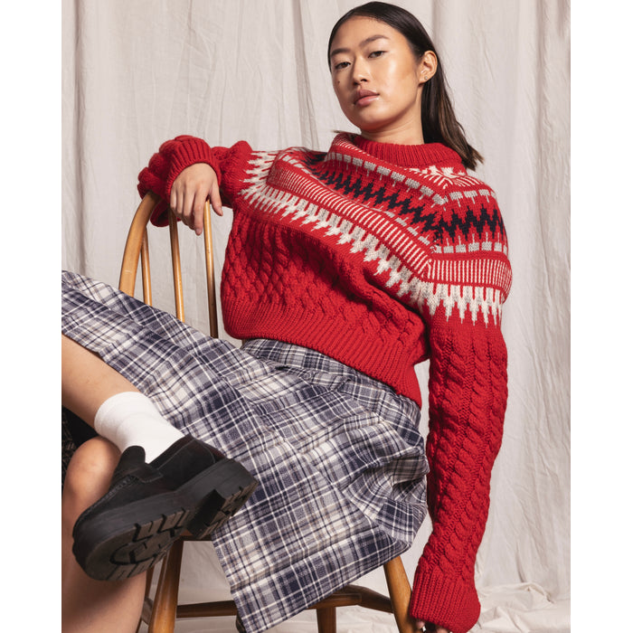Flatlay image of a red cable knitted, full length sleeve and crew neck jumper. The top half of the jumper has white, light grey and navy horizontal nordic knit patterns.