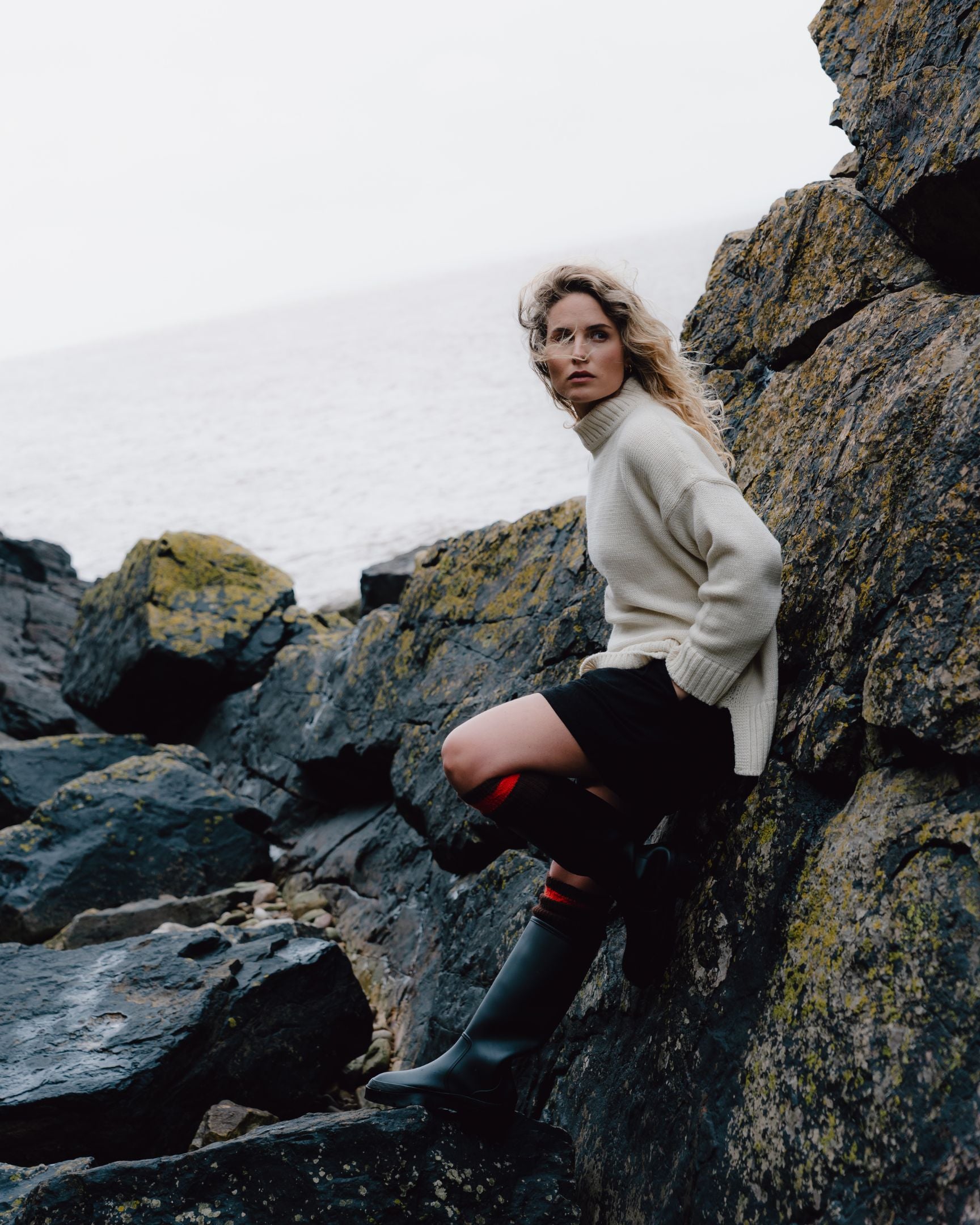 Woman in a cream sweater and black pants standing on rocky terrain