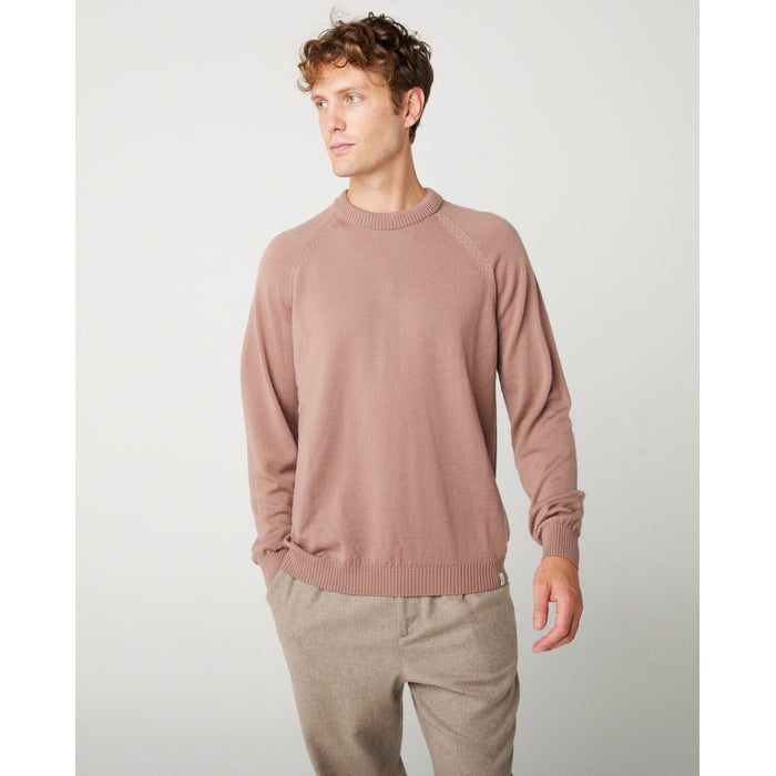 A flatlay image of a cream/ oatmeal coloured crew neck jumper. The jumper has a fine knit with a ribbed hem, cuff and neckline.  A close up photo of a male model wearing the jumper while looking to the right.  The male model is wearing the jumper and looking straight ahead.