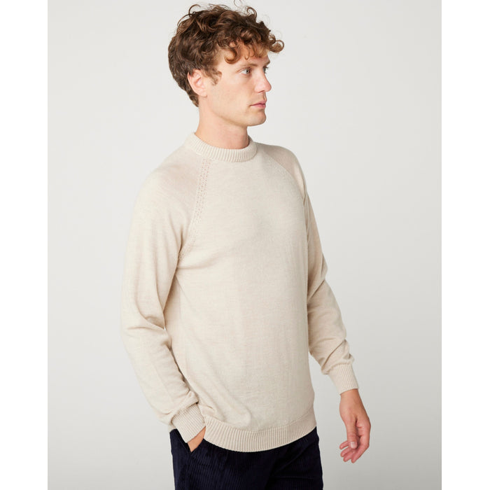 A flatlay image of a cream/ oatmeal coloured crew neck jumper. The jumper has a fine knit with a ribbed hem, cuff and neckline.  A close up photo of a male model wearing the jumper while looking to the right.  The male model is wearing the jumper and looking straight ahead.