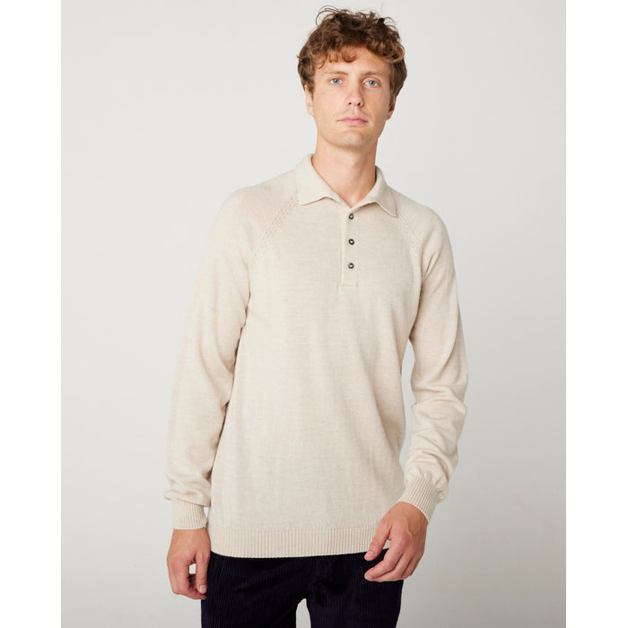 A flatlay image of a beige/ oatmeal polo shirt jumper. The jumper has a collar and  4 buttons to the chest. The hem and cuff have a ribbed detail. The jumper is a light weight, fine knit jumper and only one colour all over. A male model wearing the beige jumper with beige trousers and black shoes. He is smiling at the camera and has one hand in his trouser pocket.