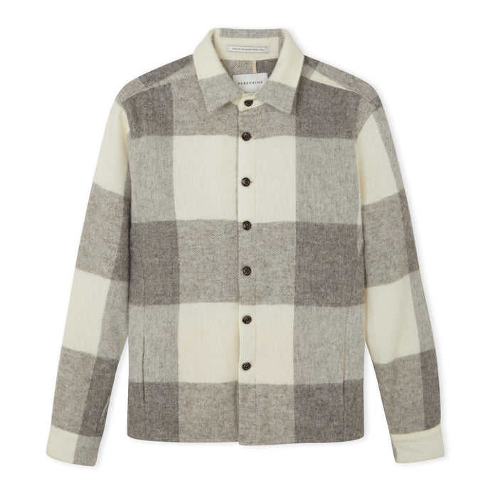 Flatlay image of a checked wool collared shirt consisting of a light grey, slightly darker grey and cream with seven small black buttons fastening down the center front fastening the shirt closed, the shirt has two discreet pockets on the either front bottom side of the shirt.